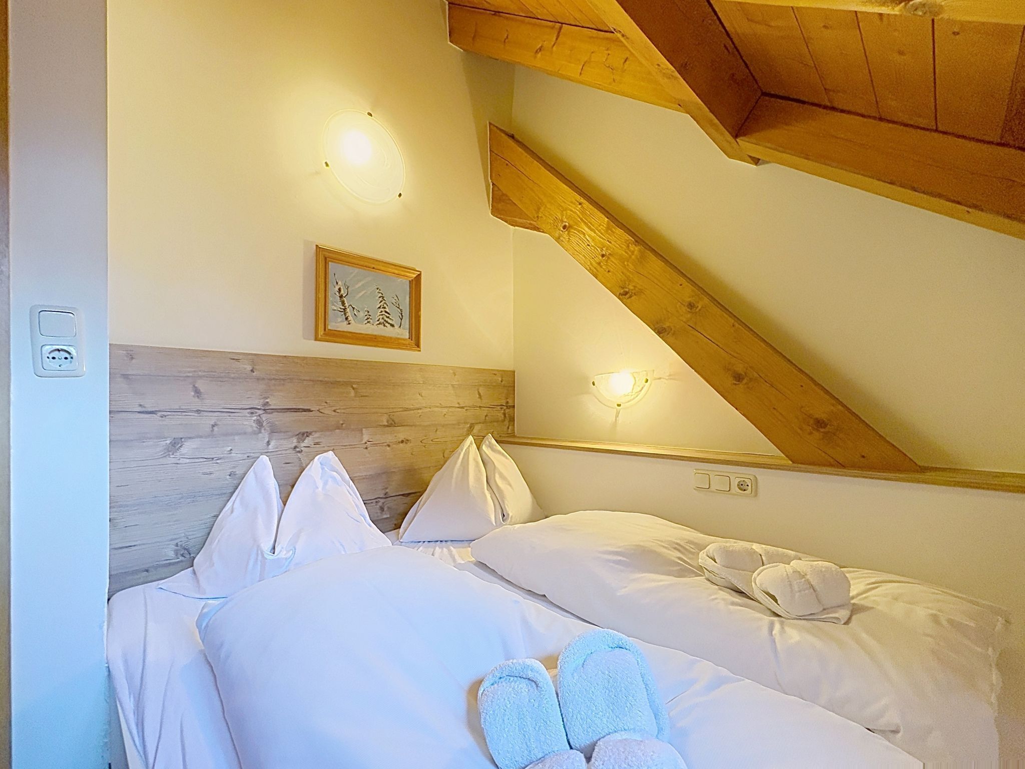 Un dormitorio con cabecera de madera, cama con ropa blanca, un cuadro en la pared y una lámpara en el techo.