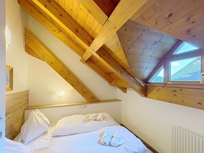 Une chambre avec un plafond en pente, un puits de lumière et un lit avec des oreillers et une serviette pliée.