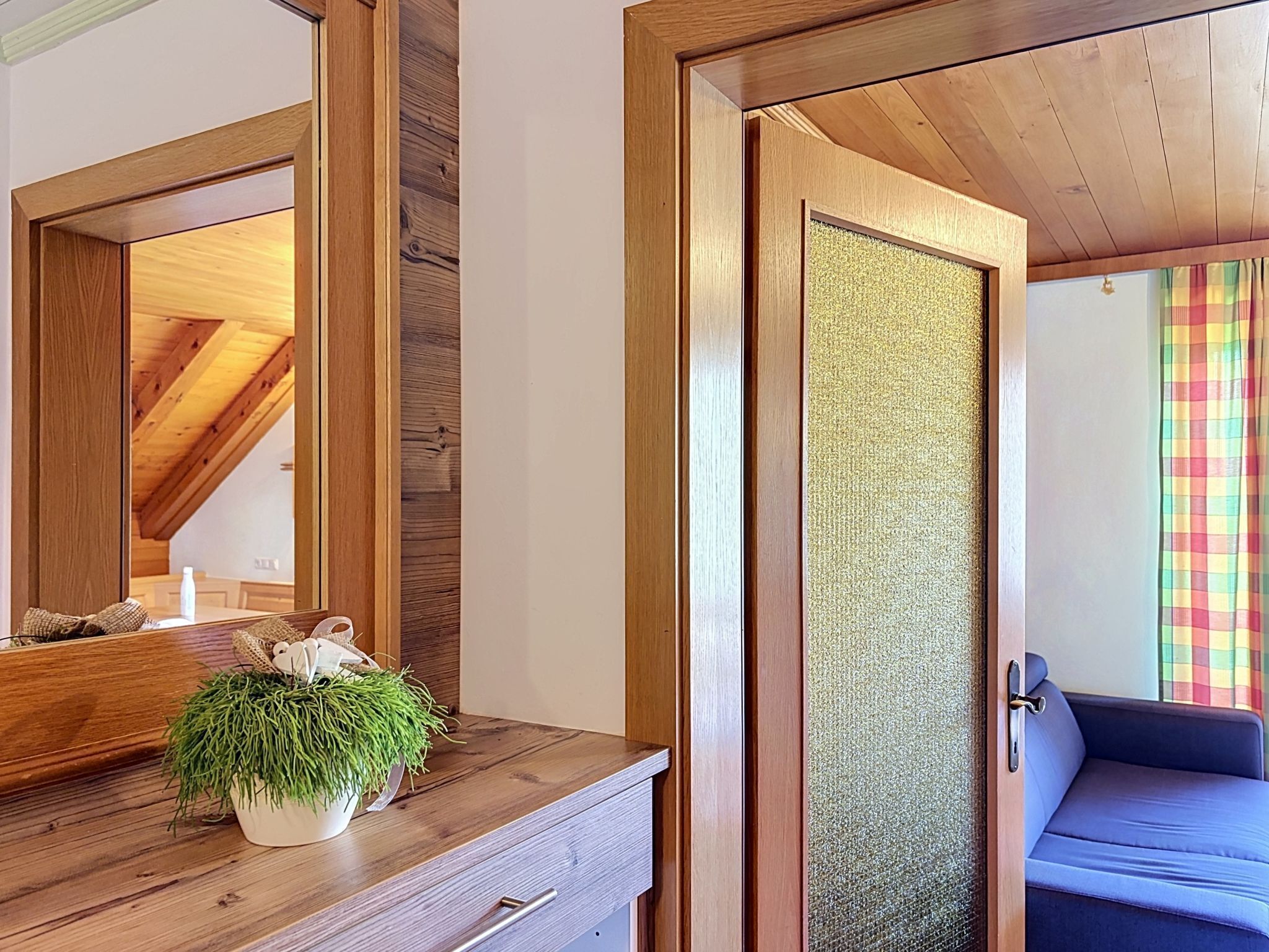 Ein Zimmer mit Holzboden, einem großen Spiegel, einer Holzkommode, einer Topfpflanze und einem blauen Sofa.