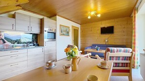 A cozy cabin interior with wooden walls, a kitchen area, a dining table with cups and a pitcher, and a sofa with a colorful blanket. - Katschberg 26 by Interhome (Sankt Michael im Lungau)
