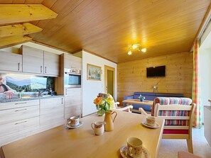 A cozy cabin interior with wooden walls, a kitchen area, a dining table with cups and a pitcher, and a sofa with a colorful blanket. - Katschberg 26 by Interhome (Sankt Michael im Lungau)