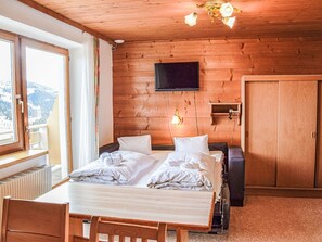 Dormitorio con paneles de madera, una cama, un televisor y una ventana con vistas a las montañas.