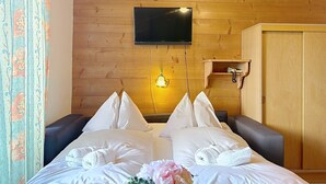 A hotel room with a wooden ceiling, a flat-screen TV mounted on the wall, a bedside table with a lamp, and a wardrobe. - Katschberg 25 by Interhome (Sankt Michael im Lungau)