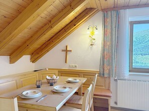 A dining area with a wooden table set for four, a cross on the wall, and a window with curtains. - Katschberg 25 by Interhome (Sankt Michael im Lungau)