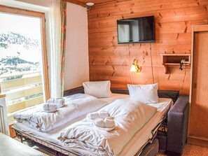 Una habitación de cabaña de madera con una cama, un televisor montado en la pared y una ventana con vista a la montaña.