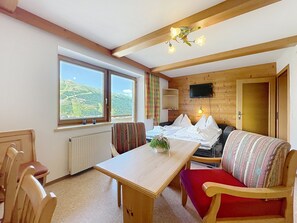 A cozy room with a wooden table, a sofa, a TV mounted on the wall, and a window with a mountain view. - Katschberg 23 by Interhome (Sankt Michael im Lungau)