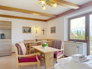 A cozy room with a wooden dining table, chairs, a bed with white linens, a window with a view of trees, and a cross on the wall. - Katschberg 23 by Interhome (Sankt Michael im Lungau)