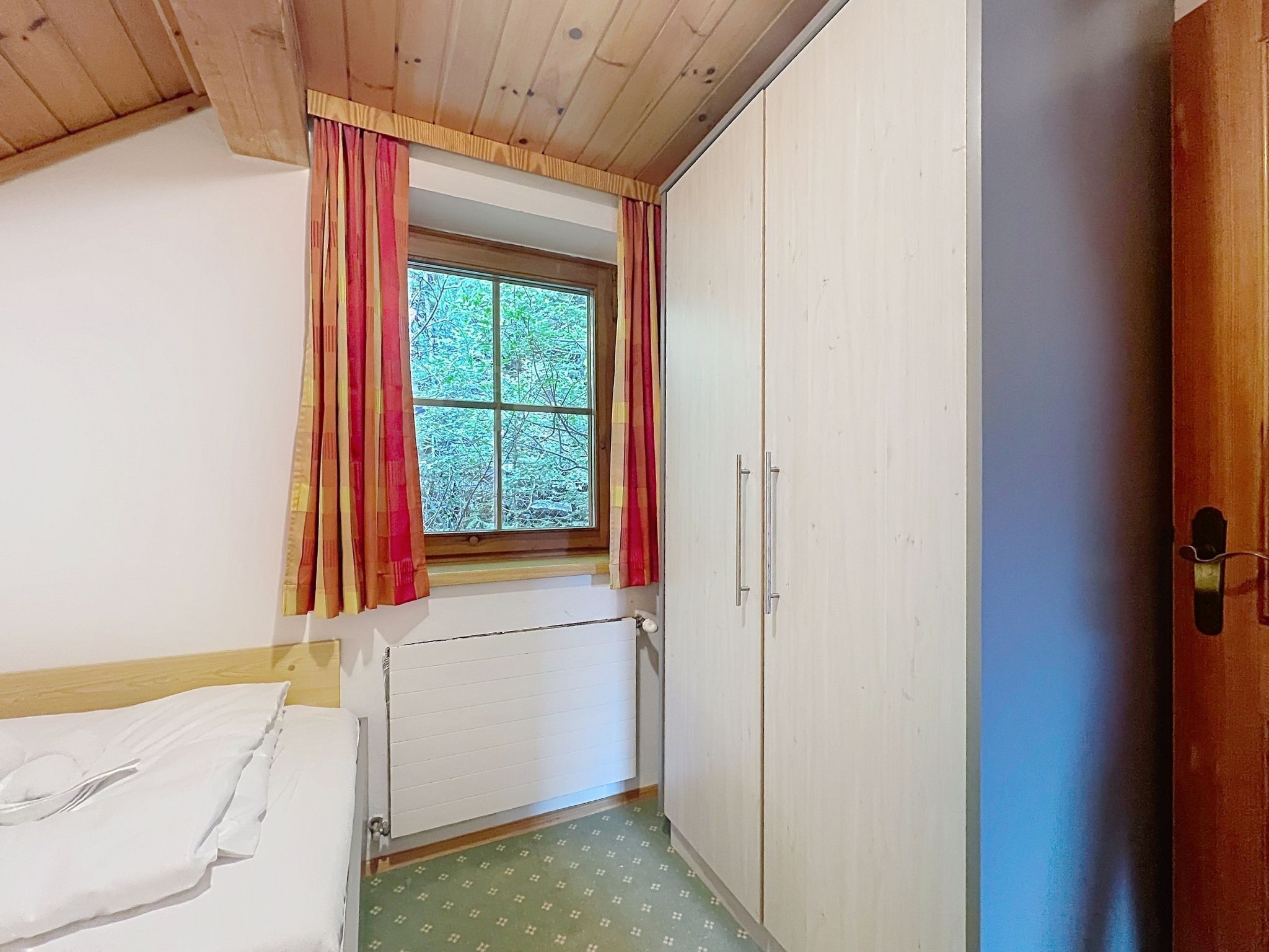 A small room with a window, a radiator, a wardrobe, and a bed.