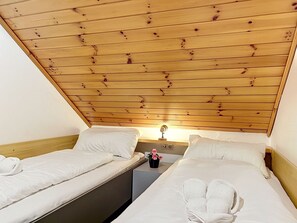 A room with two single beds, wooden headboard, a small bedside table with a lamp, and a wall-mounted power outlet. - Katschberg 21 by Interhome (Sankt Michael im Lungau)