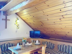 A dining area with a wooden table, benches, a cross, and a wall-mounted light fixture. - Katschberg 21 by Interhome (Sankt Michael im Lungau)