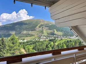 A mountain view from a balcony with a wooden railing, overlooking a town with buildings and a forested area. - Katschberg 21 by Interhome (Sankt Michael im Lungau)