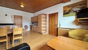 Un ambiente compatto con soffitto in legno, angolo cottura con mobili in legno, tavolo da pranzo, divano e televisore a parete.