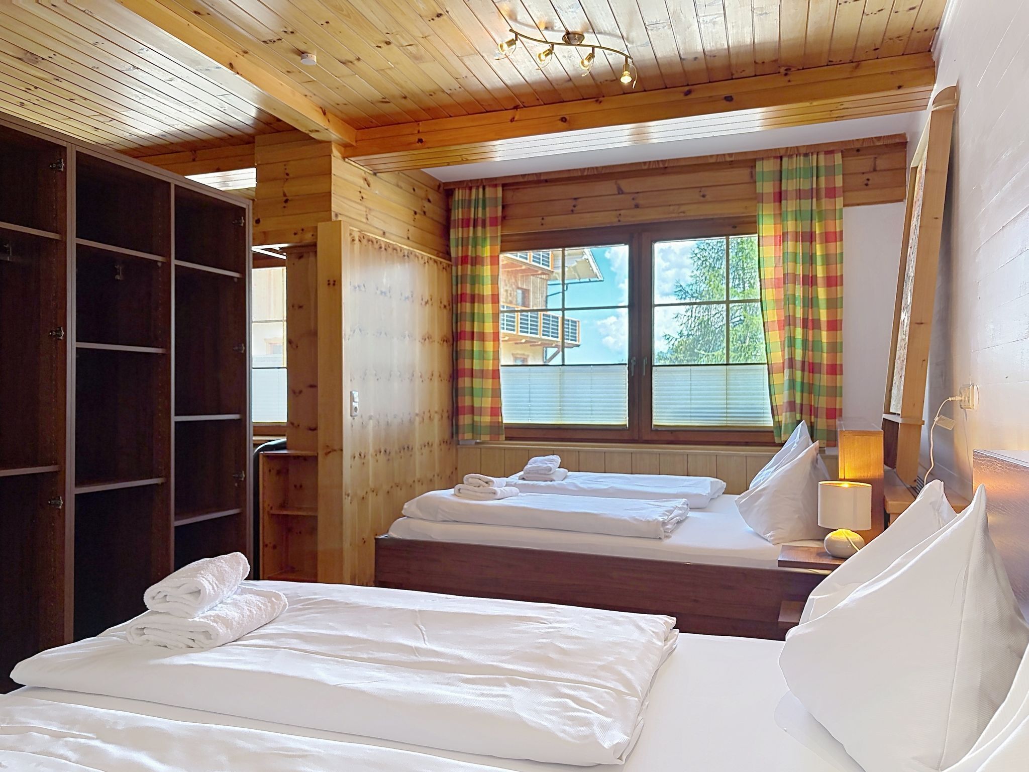 Een houten kamer met twee bedden, een kast en een raam met gordijnen.