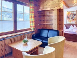 A cozy room with a wooden interior, a black leather sofa, a wooden table with a plant, and a bed with white bedding. - Katschberg 16 by Interhome (Sankt Michael im Lungau)