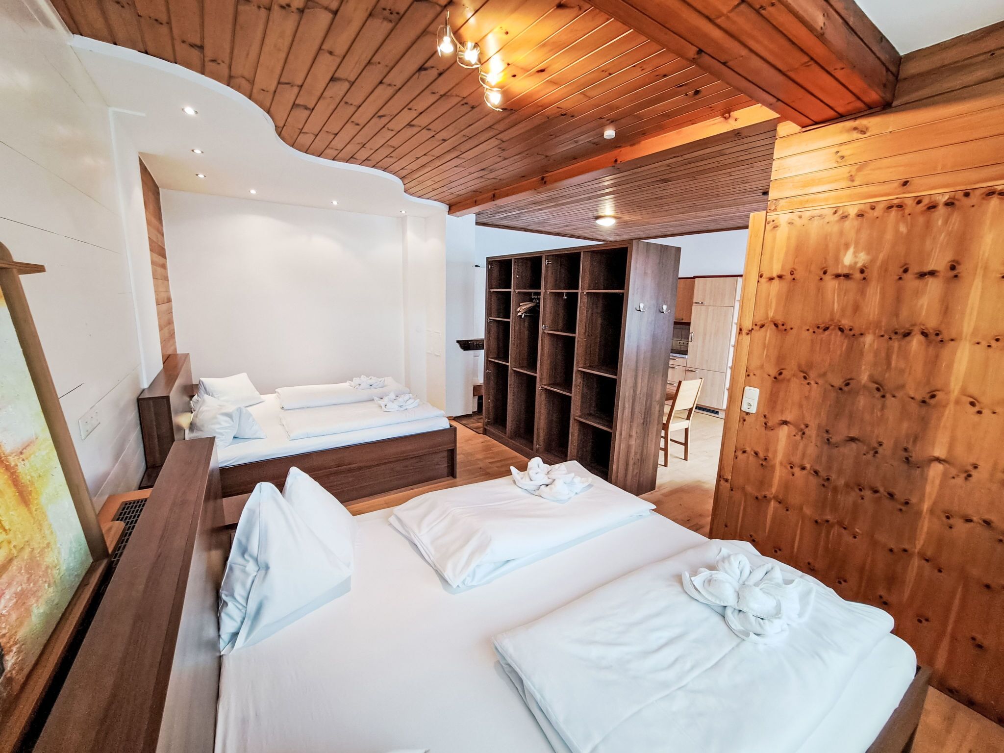 Une chambre d’hôtel moderne avec un plafond et des murs en bois, un grand lit avec du linge de lit blanc, un plus petit lit et une armoire en bois.