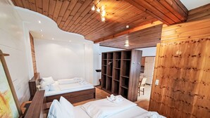 Camera d'albergo moderna con soffitto e pareti in legno, un letto grande con lenzuola bianche, un letto più piccolo e un'armadio in legno.