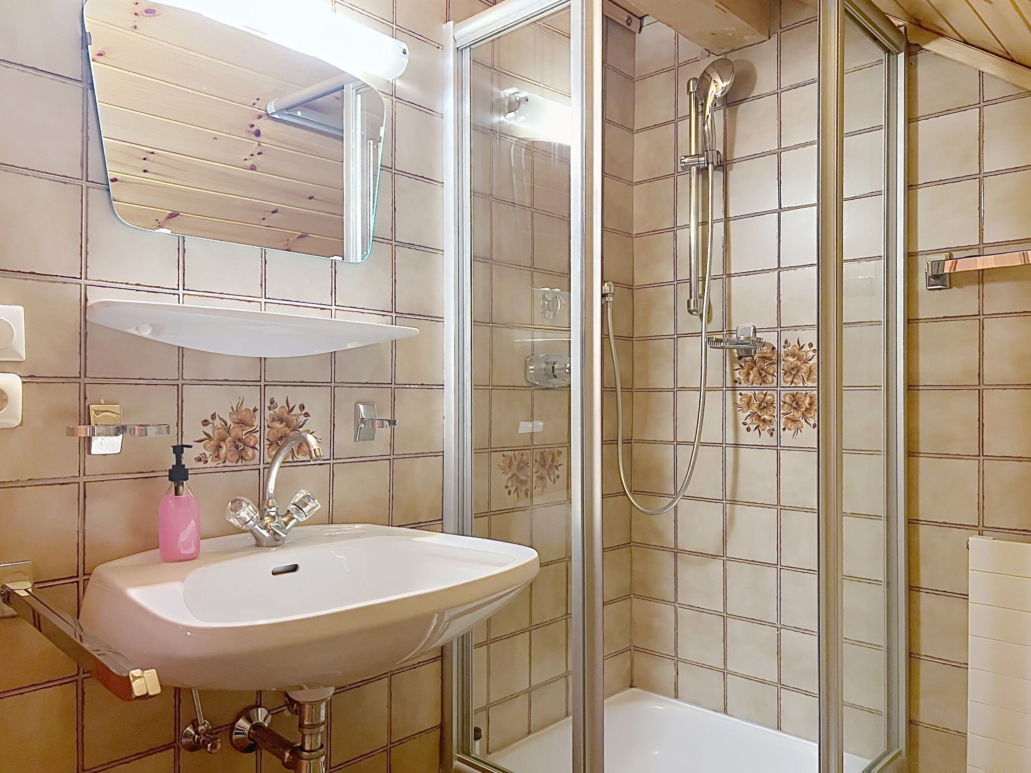 A bathroom with a sink, mirror, shower, and tiled walls.