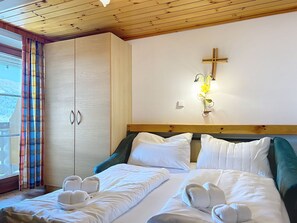 A hotel room with a bed, pillows, a cross on the wall, and a window with curtains. - Katschberg 20 by Interhome (Sankt Michael im Lungau)