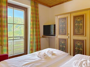 A hotel room with a bed, a television on a stand, and a view of a mountainous landscape through a window. - Katschberg 18 by Interhome (Sankt Michael im Lungau)