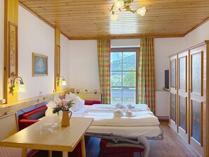 Une chambre d’hôtel avec un plafond en bois, un lit avec du linge de maison blanc, une table avec un vase de fleurs et une fenêtre avec des rideaux.