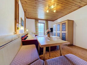 Une pièce avec un plafond en bois, une table à manger, des bancs, un buffet orné de panneaux décoratifs et une fenêtre avec des rideaux.
