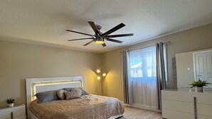 A bedroom with a bed, bedside tables, a ceiling fan, a large window with curtains, and a dresser. - Modern home away from home in Courtice (Courtice)