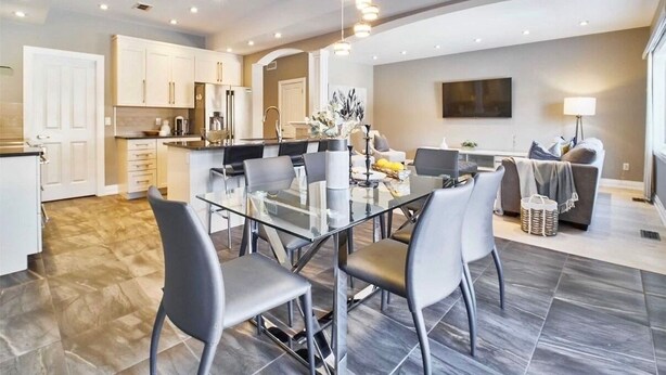 A modern kitchen with white cabinets, a dining area with a glass table, and a living room with a sofa and TV. - Modern home away from home in Courtice (Courtice)