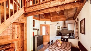 Una cuina rústica amb bigues de fusta, una taula de menjador amb mantell a escac i taula, i una escala que condueix a una altra habitació.