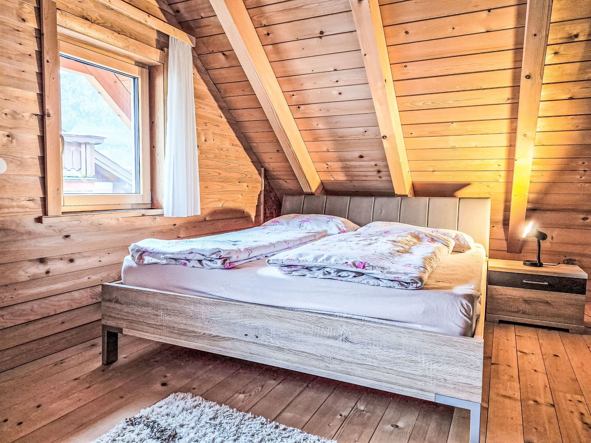 A wooden cabin bedroom with a bed, a nightstand, a lamp, and a window.