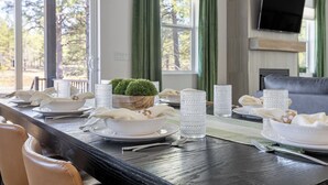 Una mesa de comedor dispuesta con platos, tazones y servilletas blancos, una pequeña planta en maceta y copas altas con textura.