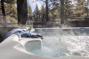A hot tub with a glass of white wine and a towel, surrounded by trees. - Luxe Mountain Escape Hot Tub & Pool Table (Flagstaff)
