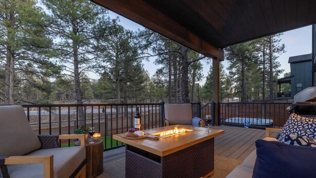 Un espacio de estar techado al aire libre con chimenea, sillas y vistas del bosque circundante.