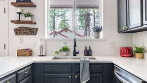 A modern kitchen with dark cabinets, a white countertop, a window with a view of trees, and a red toaster. - Flagstaff Retreat with Hot Tub (Flagstaff)