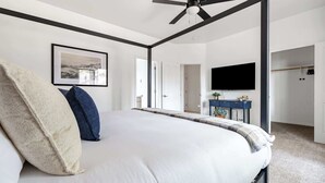 A bedroom with a bed, a ceiling fan, a framed picture on the wall, a TV mounted above a blue console table, and a door leading to another room. - Flagstaff Retreat with Hot Tub (Flagstaff)