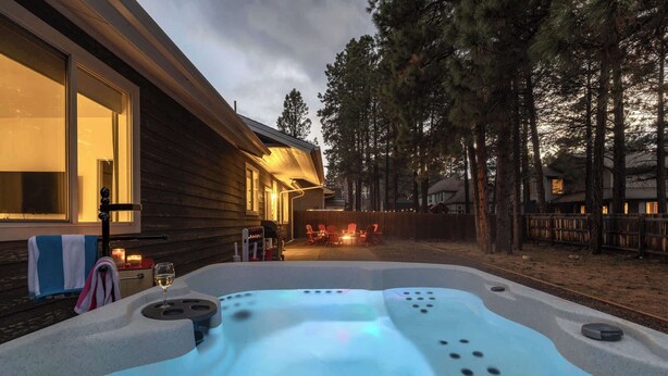 A hot tub in a backyard with a wooden house and a fire pit in the background. - Flagstaff Retreat with Hot Tub (Flagstaff)