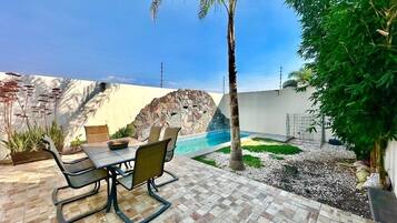 Une terrasse avec une table et des chaises, une petite piscine et un mur d’escalade.