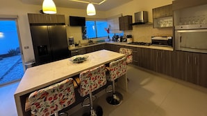 Een moderne keuken met een centraal kookeiland, barstoelen, roestvrijstalen apparatuur en hanglampen.