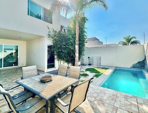 Une terrasse extérieure moderne avec une piscine, une table à manger avec des chaises et un petit coin jardin.