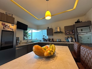 Une cuisine moderne dotée d’un plan de travail en marbre, d’un panier de fruits et d’un luminaire suspendu.