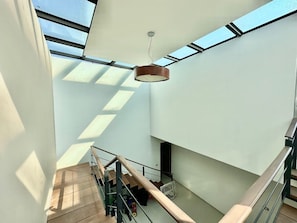 Un intérieur moderne avec un escalier, des puits de lumière et un luminaire suspendu.