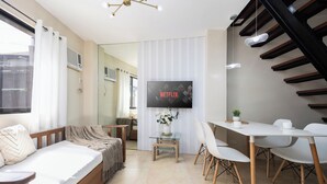 Une chambre d’hôtel moderne comprenant un lit, un coin repas avec une table et des chaises, un téléviseur fixé au mur et un escalier.