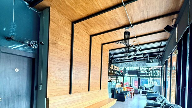 A modern interior with a long wooden bench, leather seating, and a view of bicycles outside. - Karat Residence (Pattaya)