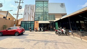 A modern building with a prominent logo, a covered entrance, and several parked motorcycles. - Karat Residence (Pattaya)