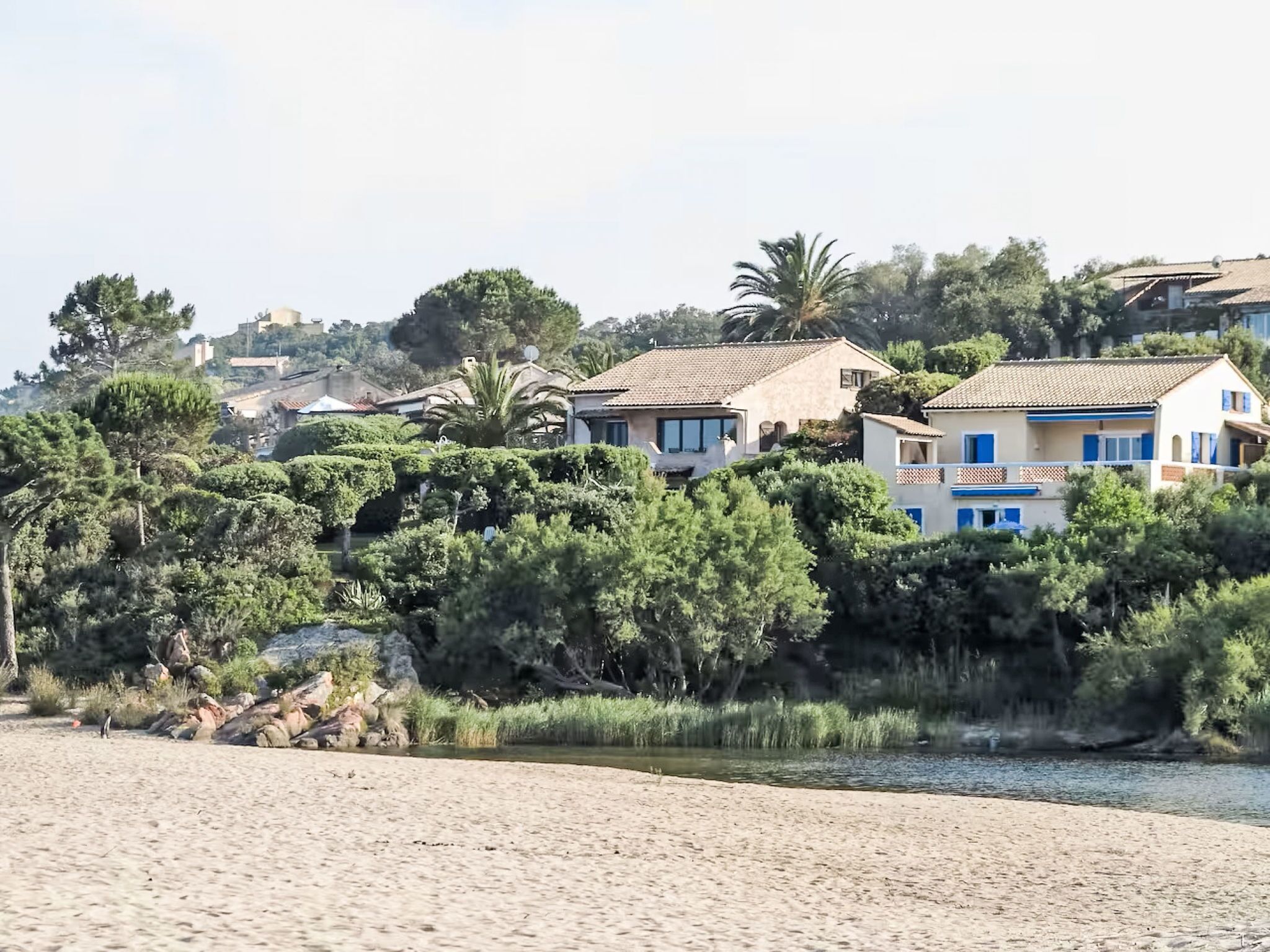 Ein Küstengebiet mit mediterranen Häusern, üppiger Vegetation und einem Sandstrand.