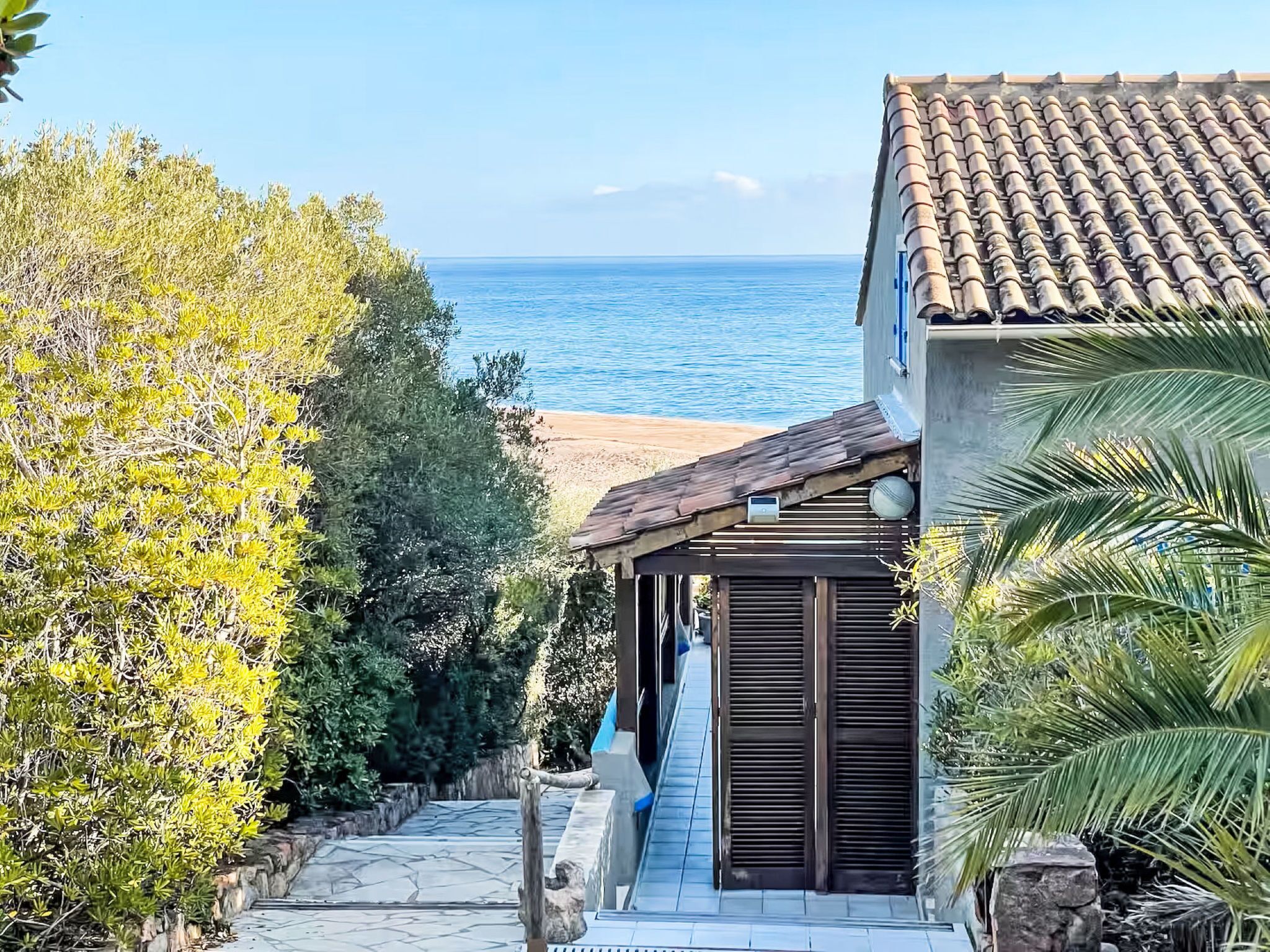 Ein Küstengebiet mit einem Kiesweg, der zu einer Holztür führt, mit Blick auf einen Strand und das Meer.