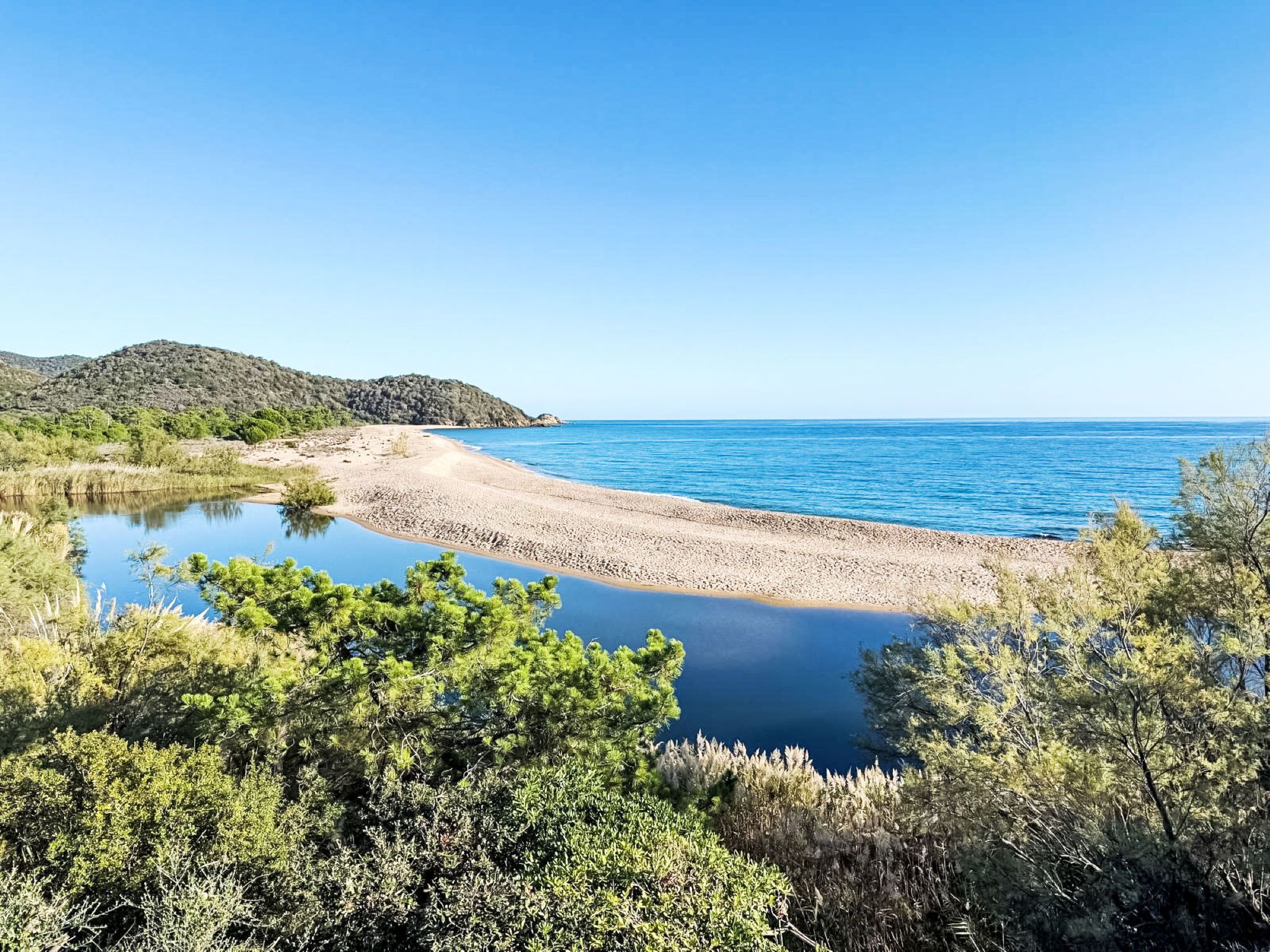 Un paisaje costero con playa, mar tranquilo y vegetación circundante.