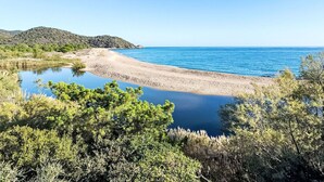 Paesaggio costiero con spiaggia, mare calmo e vegetazione circostante.