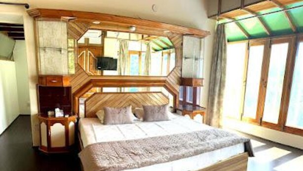 Quarto espaçoso com cama grande, cabeceira de madeira e vista pela janela.
