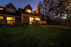 A two-story house with a front porch and a deck, surrounded by a grassy yard.