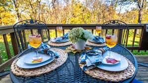 Mesa al aire libre con individuales tejidos, dos platos, una planta en maceta y dos copas de vino.